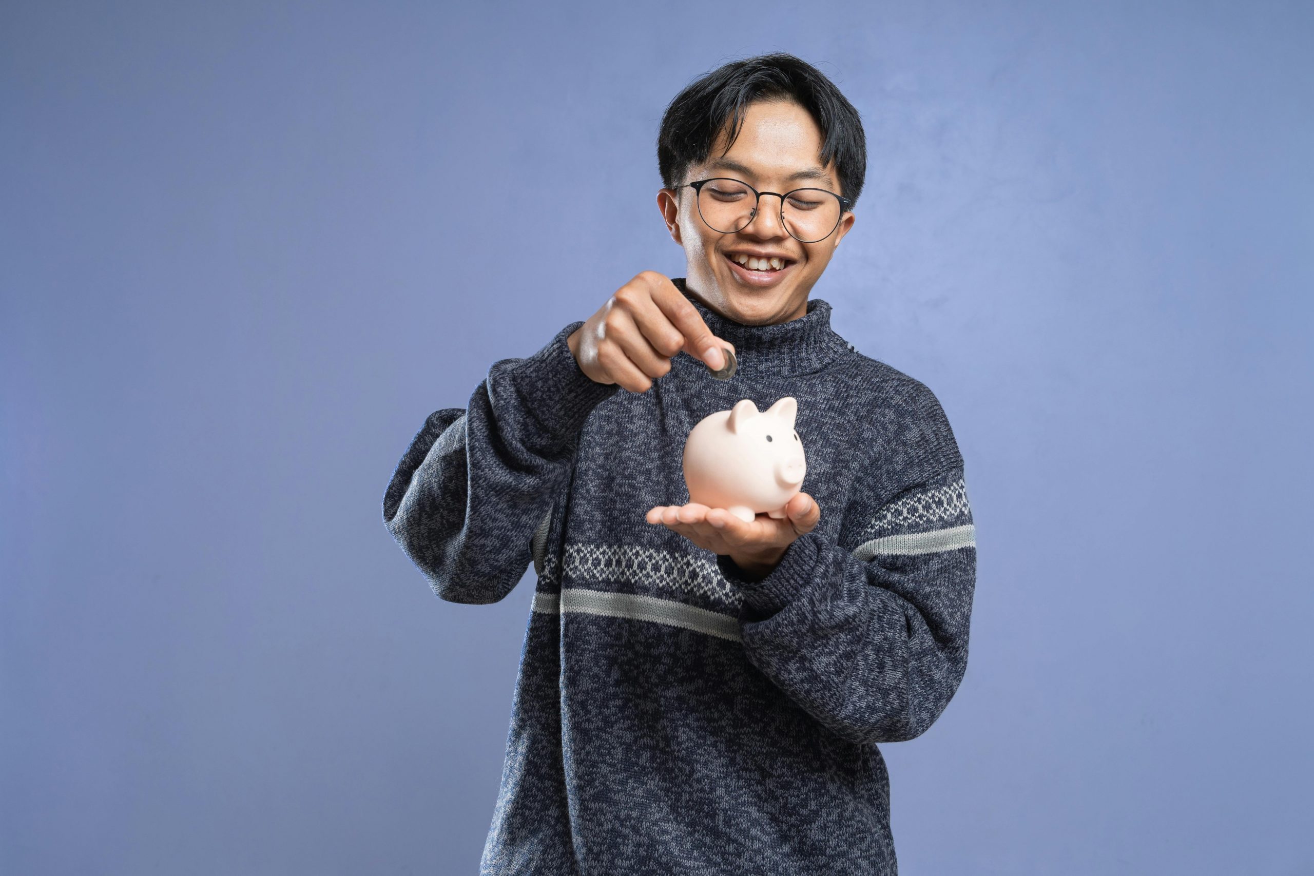 young man with glasses putting a coin into a piggy bank