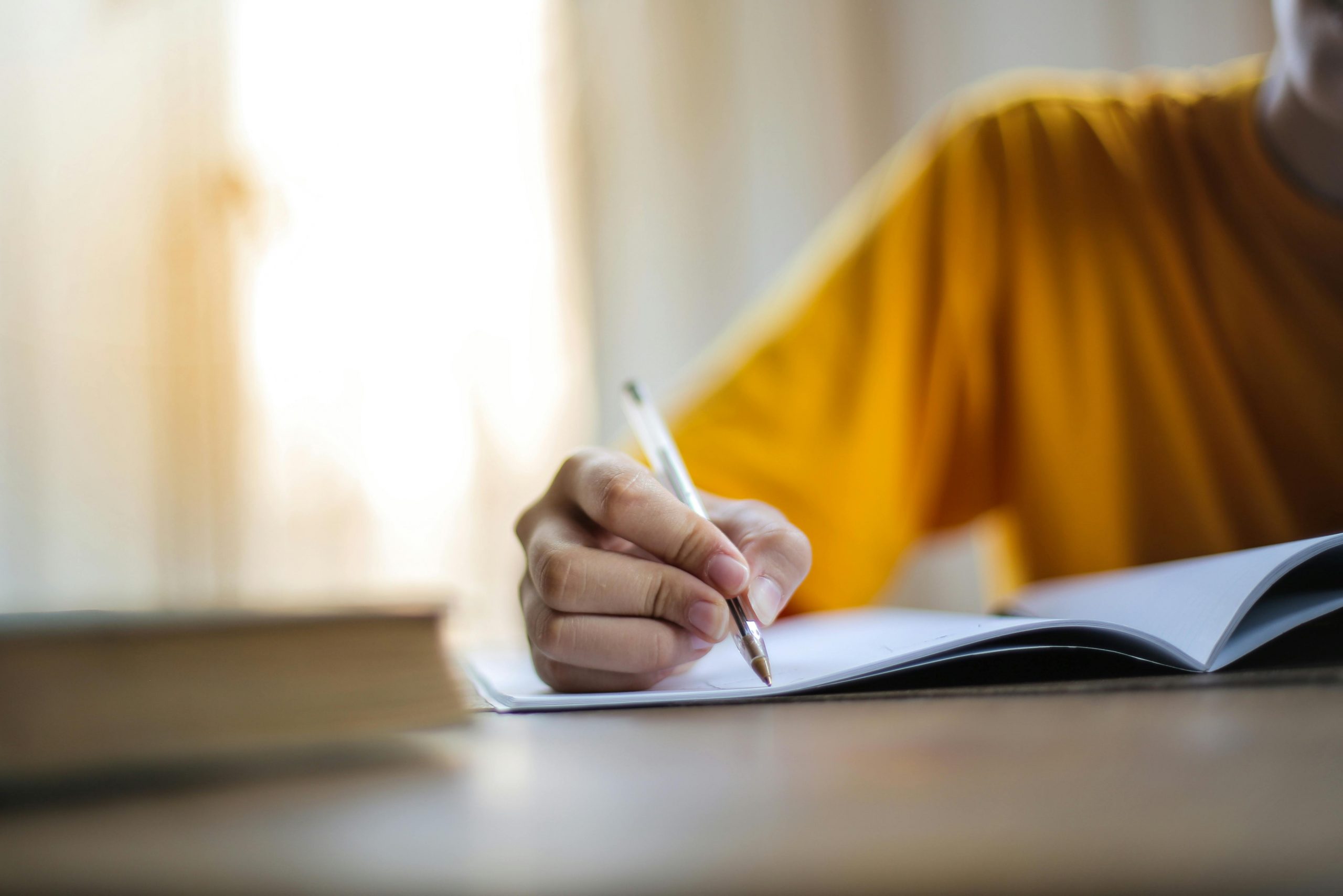 hand holding a pen, writing notes or text onto the pages of a notebook